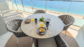 Ein runder Tisch mit Korbstühlen, gedeckt für ein Frühstück, mit Blick auf Strand und Meer.
