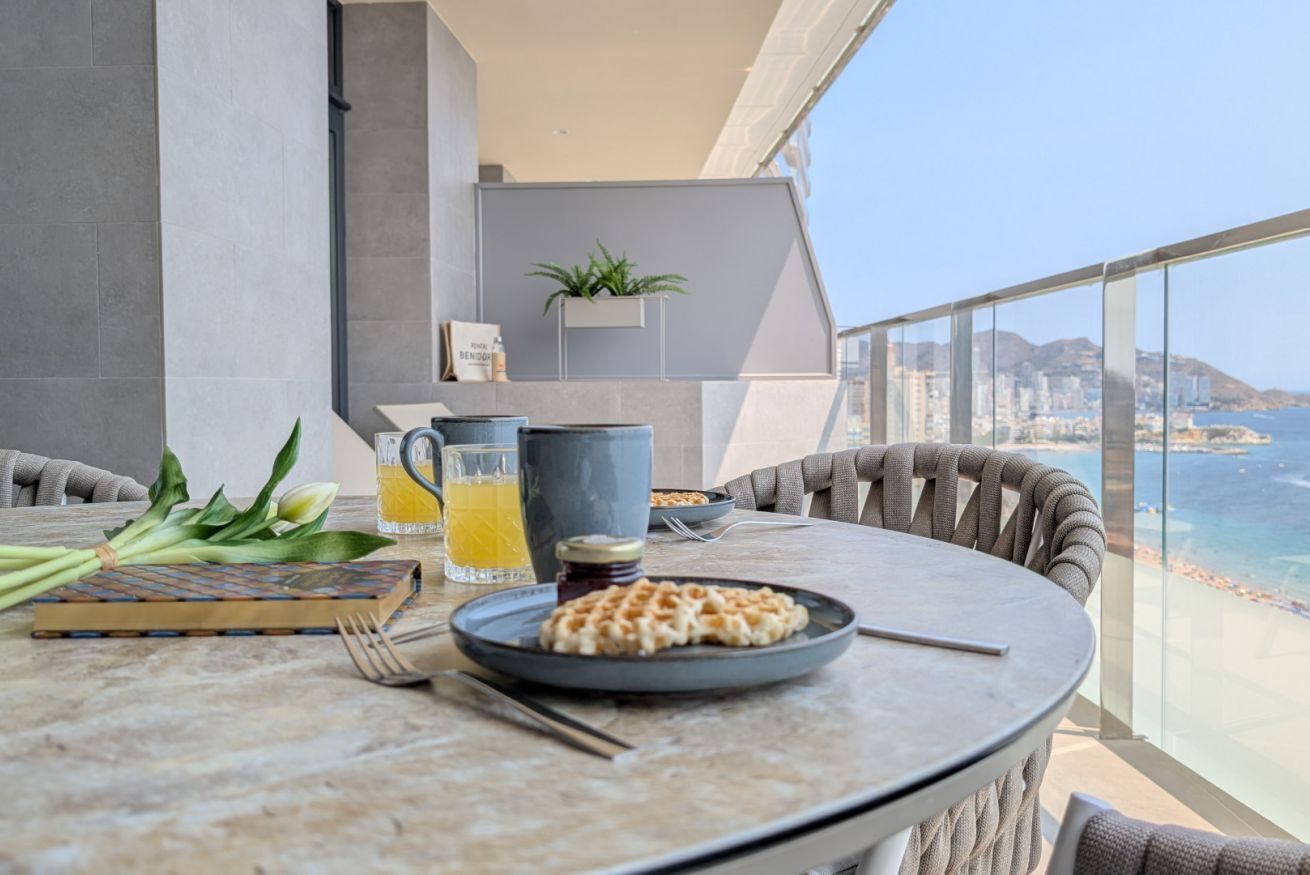 A dining table with a waffle, a pitcher of orange juice, and a bowl of cereal.