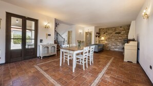 A spacious living area with a dining table, chairs, a stone wall, and a staircase. - Villa del Rio by MMega (Strettoia)
