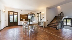 A spacious kitchen with a dining area, a staircase, and a view of the outdoors. - Villa del Rio by MMega (Strettoia)