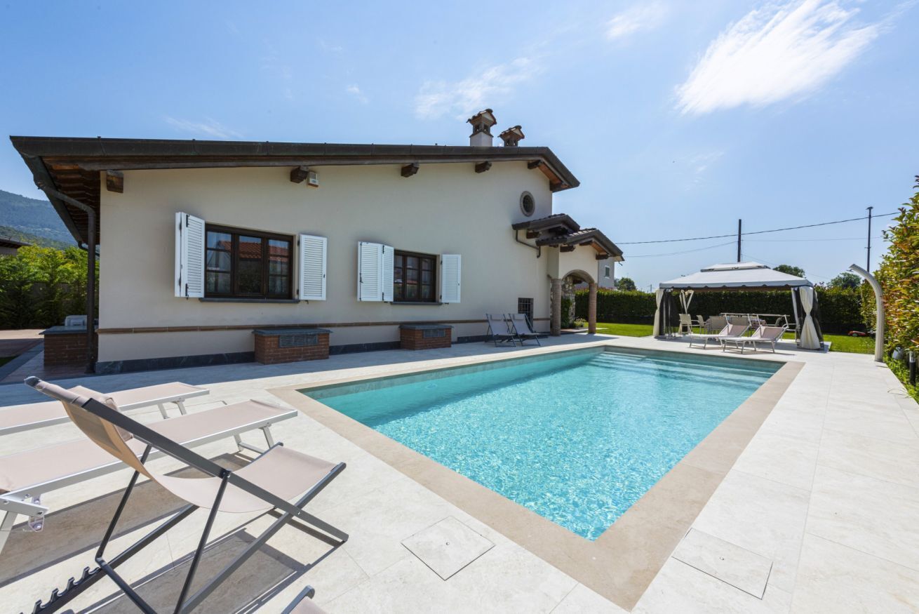 Ein Pool mit Liegestühlen, einer überdachten Sitzgelegenheit und einem Gebäude mit Fensterläden.