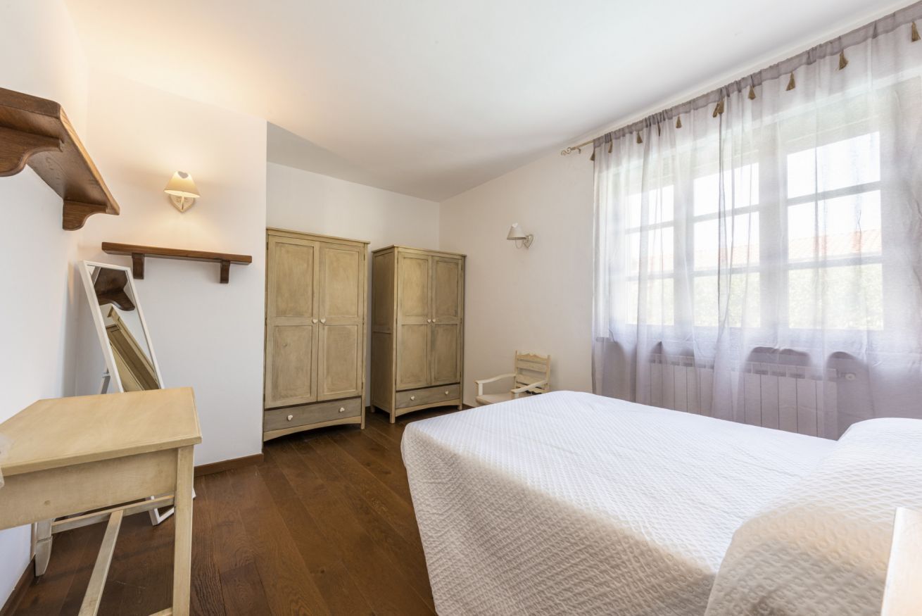 Ein Schlafzimmer mit einem Bett, Holzschränken, einem Schreibtisch und einem Fenster mit Vorhängen.