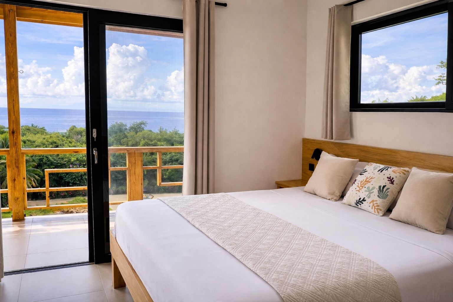 Een slaapkamer met een groot bed, een houten hoofdbord en uitzicht op de oceaan door een schuifdeur.