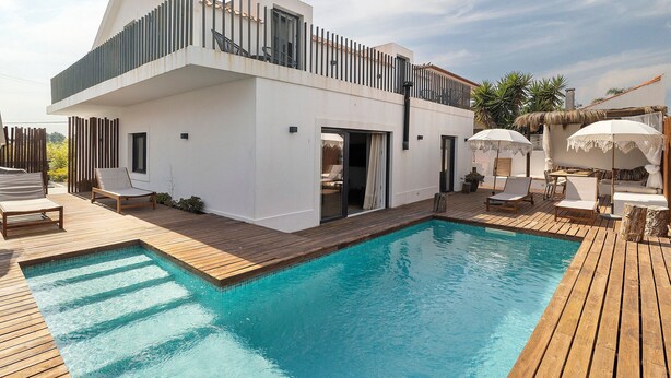 A modern two-story house with a swimming pool, wooden deck, and outdoor seating.