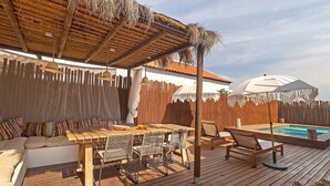 A wooden deck with a pool, a covered seating area, and a dining table with chairs.