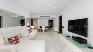 A modern living room with a sofa, a flat-screen TV, a glass coffee table, and a dining area in the background. - Palm Jumeirah 2BR Prime Burj Al Arab Balcony (Dubai)