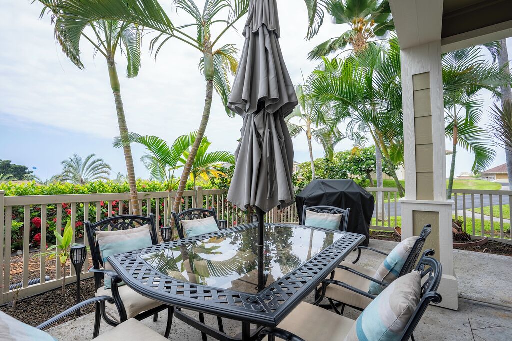 Un espace extérieur abrité, avec une table en verre, des chaises en métal et un parasol gris.
