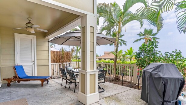 A covered patio area with a ceiling fan, a lounge chair, a table with chairs, and a grill cover. - Alii Cove II-4 | Monthly Rental in Kona | 30-Day Stay Alii Drive (Kailua Kona)