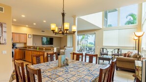 A spacious kitchen with wooden cabinets, a dining area with a patterned tablecloth, and a living area with a sofa and chairs. - Alii Cove II-4 | Monthly Rental in Kona | 30-Day Stay Alii Drive (Kailua Kona)