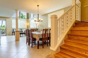 A dining area with a wooden staircase, a chandelier, and a view of the outdoors. - Alii Cove II-4 | Monthly Rental in Kona | 30-Day Stay Alii Drive (Kailua Kona)
