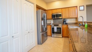A kitchen with white cabinets, stainless steel appliances, a granite countertop, and a built-in oven. - Alii Cove II-4 | Monthly Rental in Kona | 30-Day Stay Alii Drive (Kailua Kona)