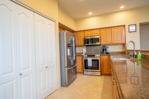 A kitchen with white cabinets, stainless steel appliances, a granite countertop, and a built-in oven. - Alii Cove II-4 | Monthly Rental in Kona | 30-Day Stay Alii Drive (Kailua Kona)