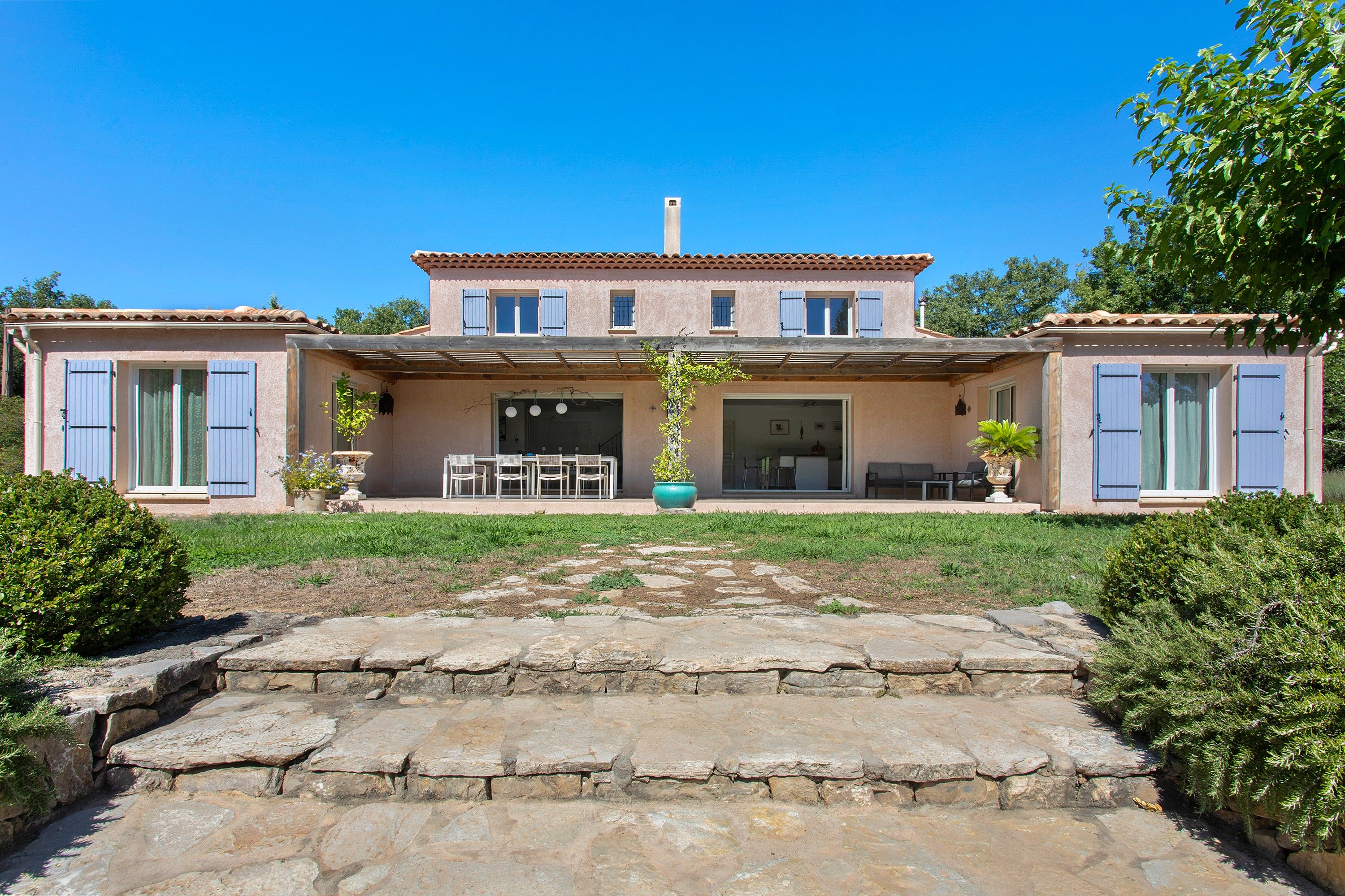 Una casa de dos pisos con un patio, comedor y jardín.