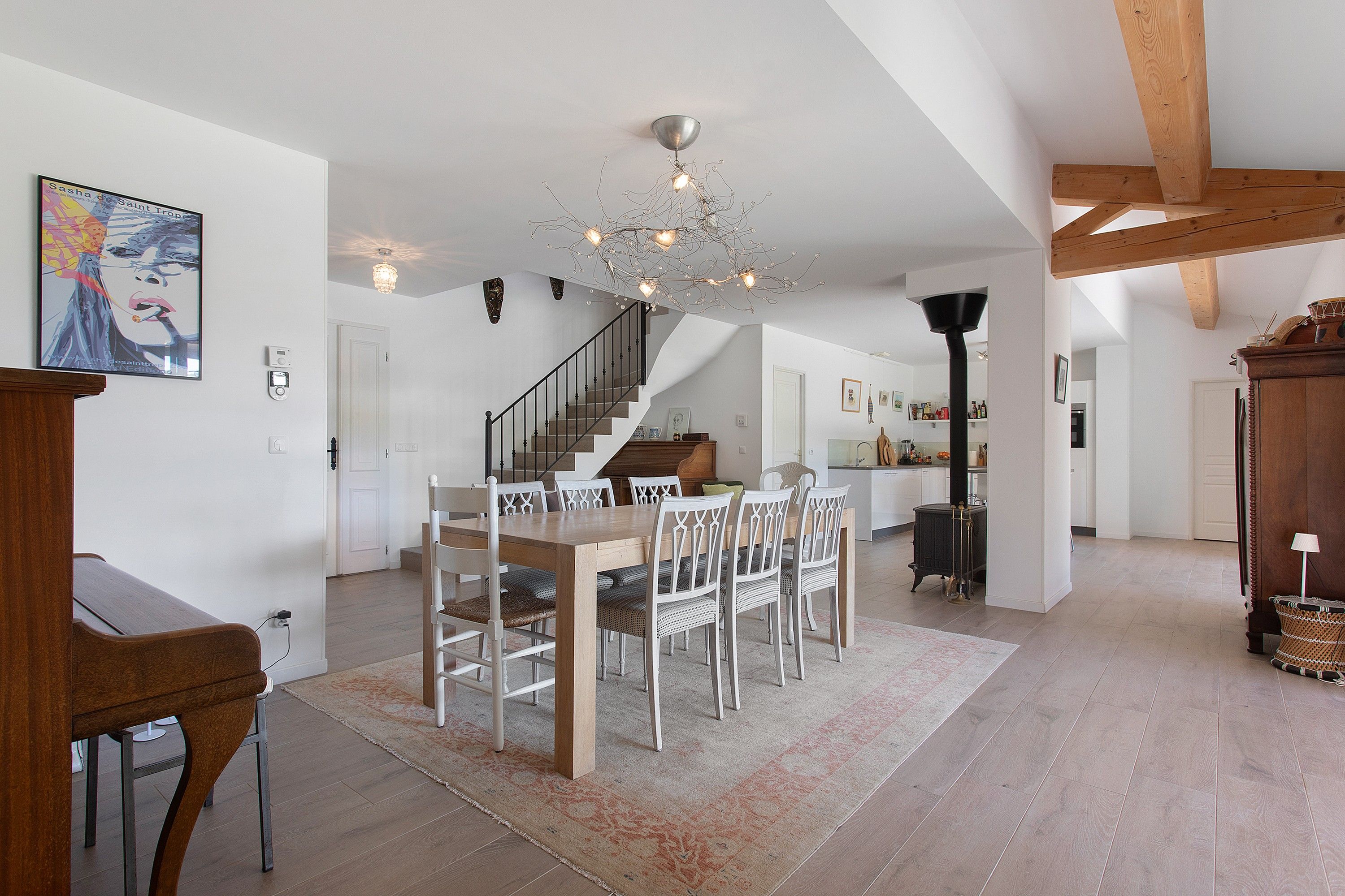 Ein geräumiger Essbereich mit Holztisch und Stühlen, eine Treppe, die in einen oberen Bereich führt, und eine moderne Chandelier.