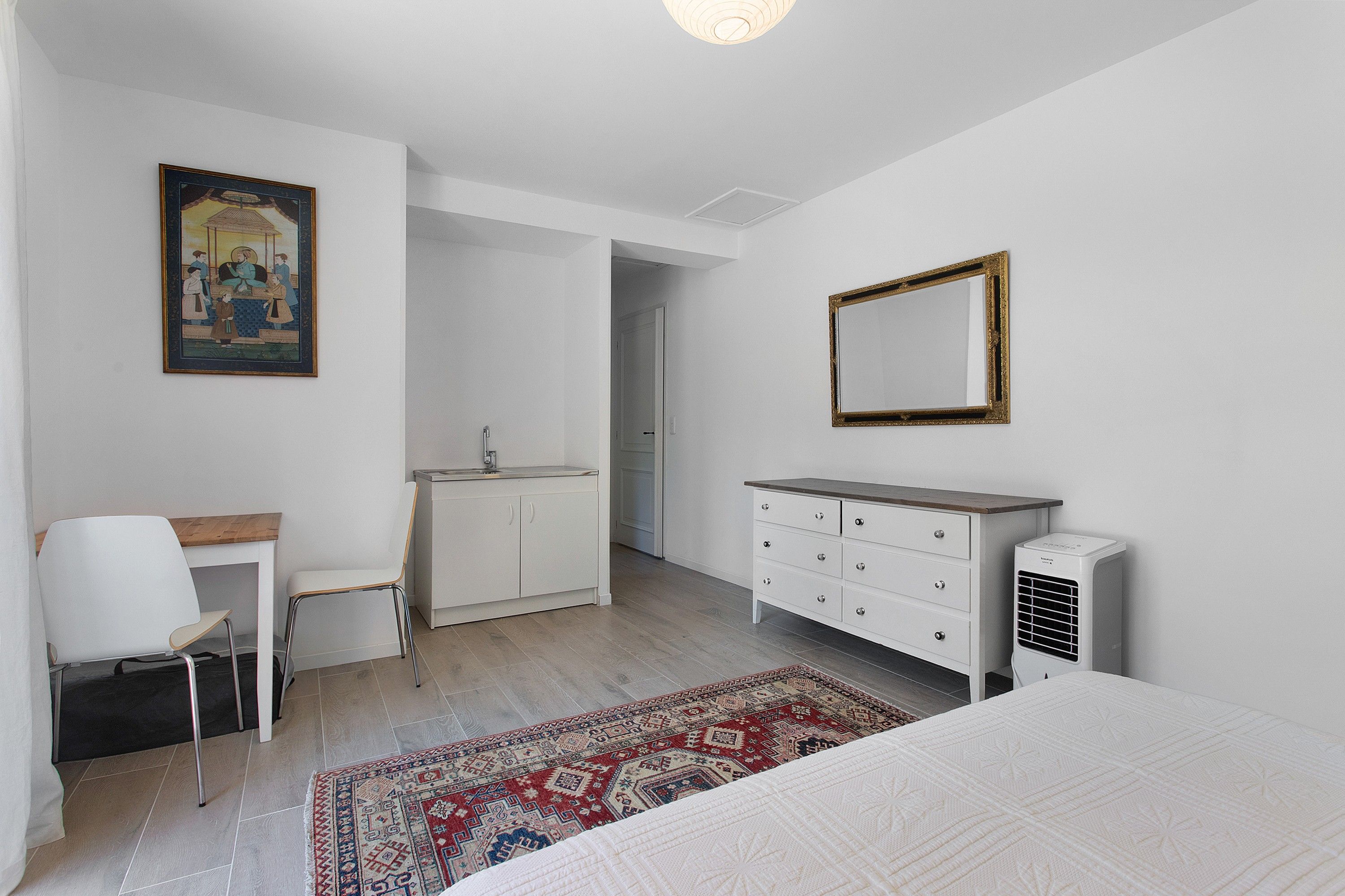 A bedroom with a bed, a bedside table, a chair, a dresser, a mirror, and a painting on the wall.
