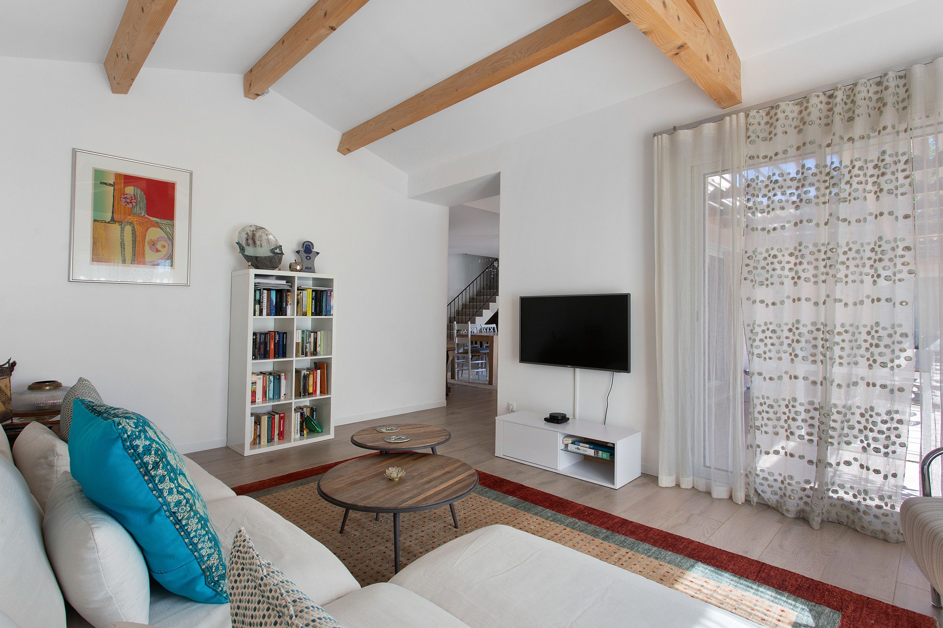 Una sala de estar con un sofá, una estantería, un televisor de pantalla plana y una escalera que sube a otro nivel.
