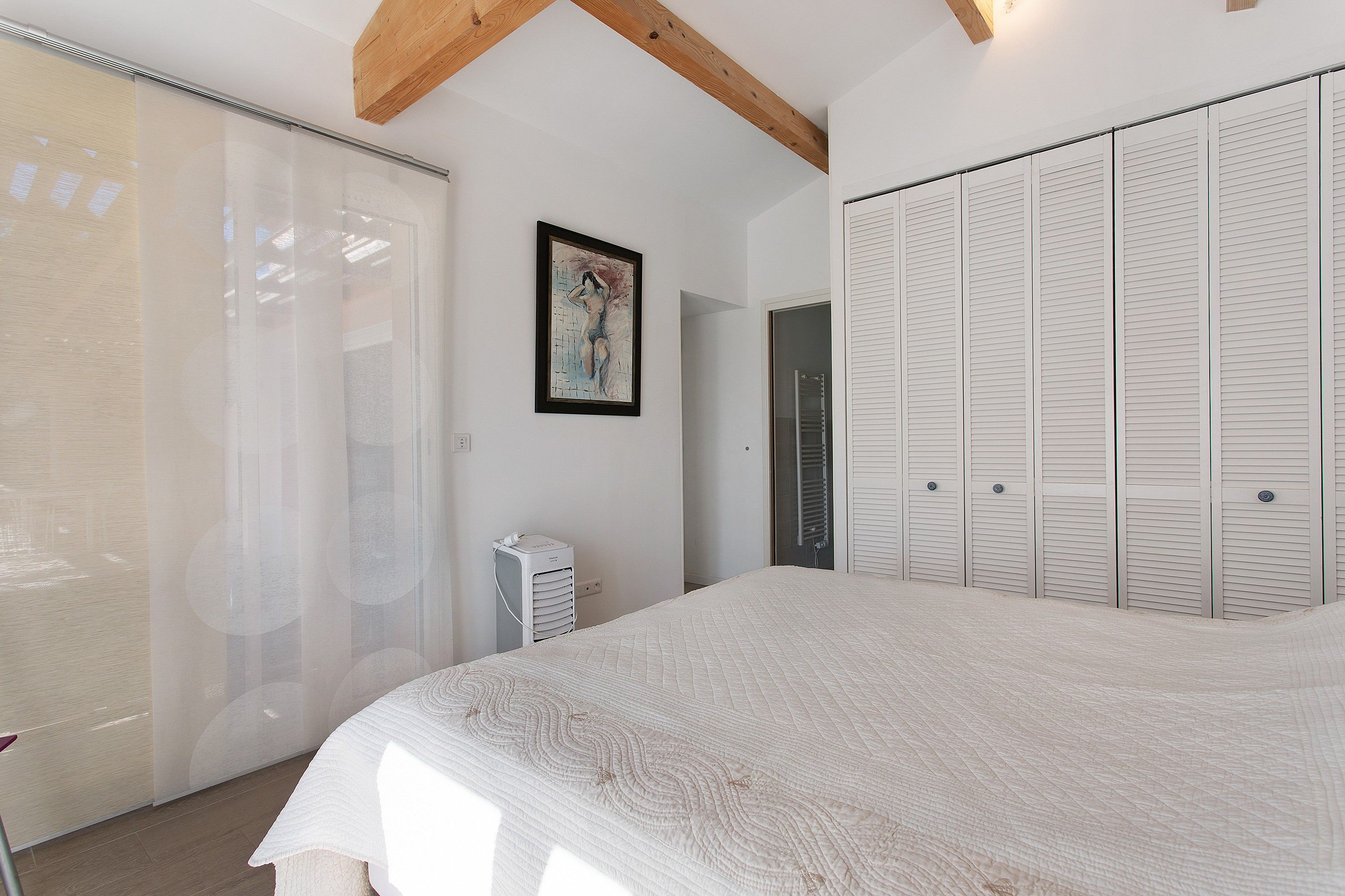 A bedroom with a bed, a wardrobe, a radiator, and a painting on the wall.