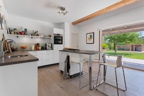 A modern kitchen with white cabinetry, a built-in oven, and a dining area with bar stools. - Villa 'Maison Mennoise' with Swimming Pool (Tourrettes)