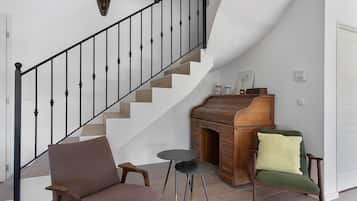 Een trap met een zwarte leuning, een houten bankje, een klein rond tafeltje en een groene fauteuil met kussens.