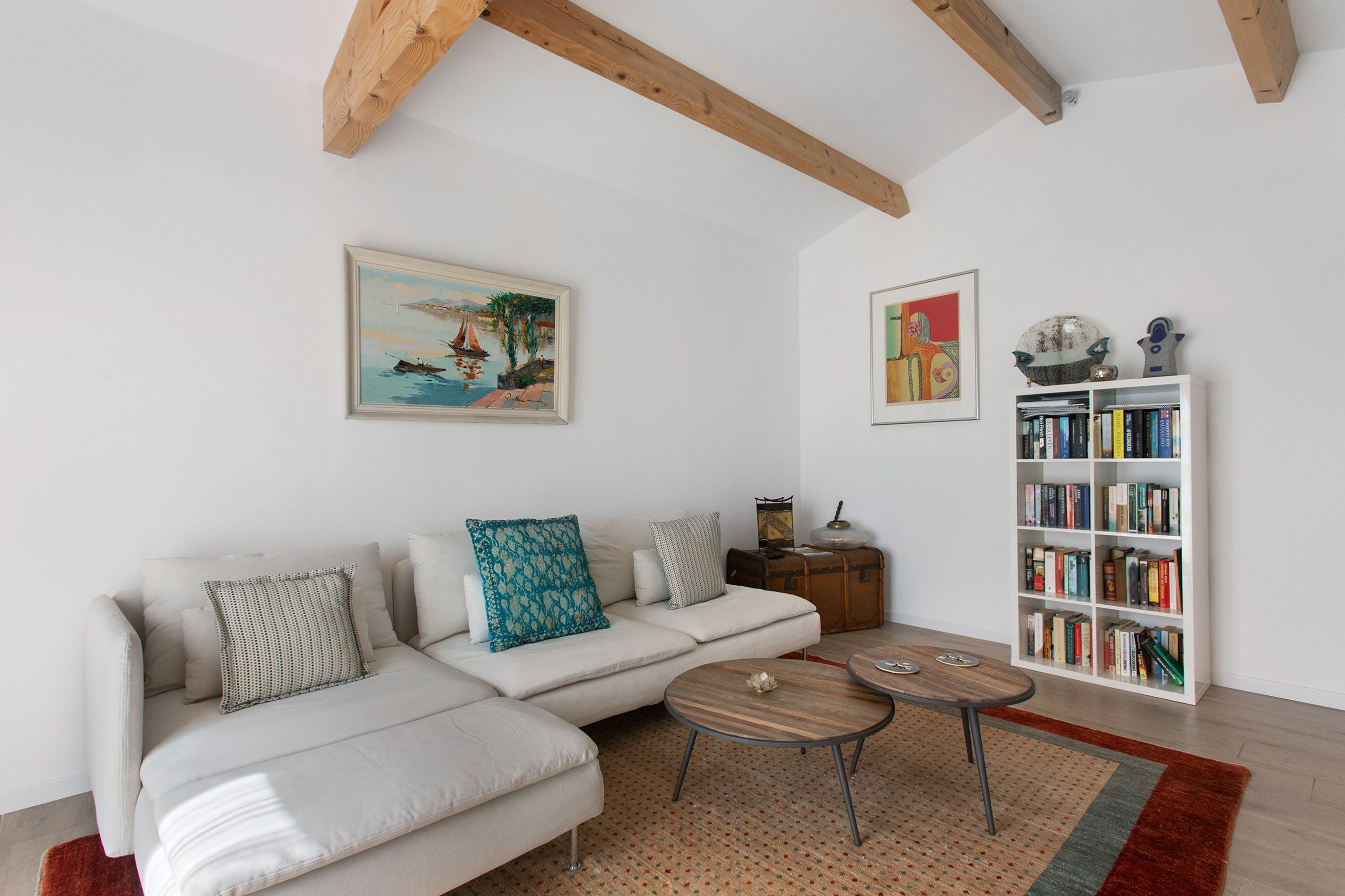 Un salon avec un canapé blanc, deux tables basses, une bibliothèque et deux œuvres d’art encadrées accrochées au mur.