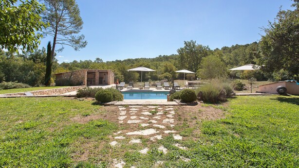 Un patio trasero con piscina, un sendero de piedra, mobiliario exterior y un edificio de piedra.
