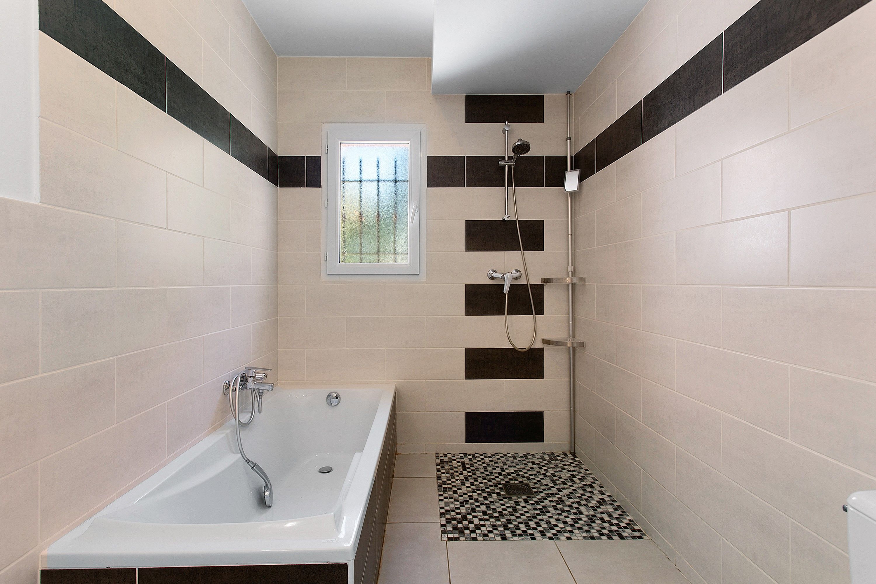 A bathroom with a bathtub, shower, and a small window.