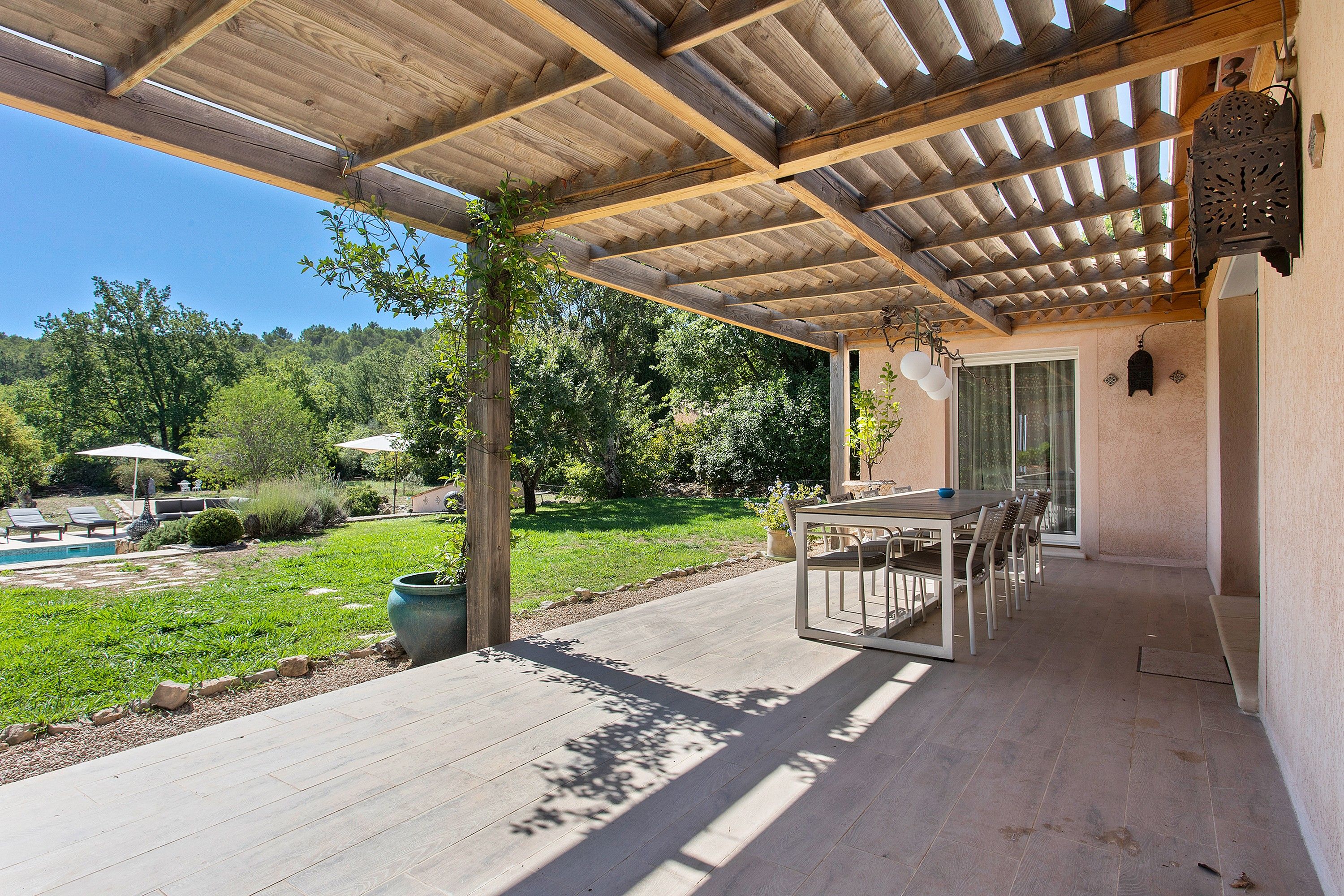 Eine überdachte Terrasse mit Tisch und Stühlen, ein Pool und ein Garten.