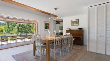 Een eetgedeelte met een houten tafel en stoelen, een kroonluchter en uitzicht op groen.