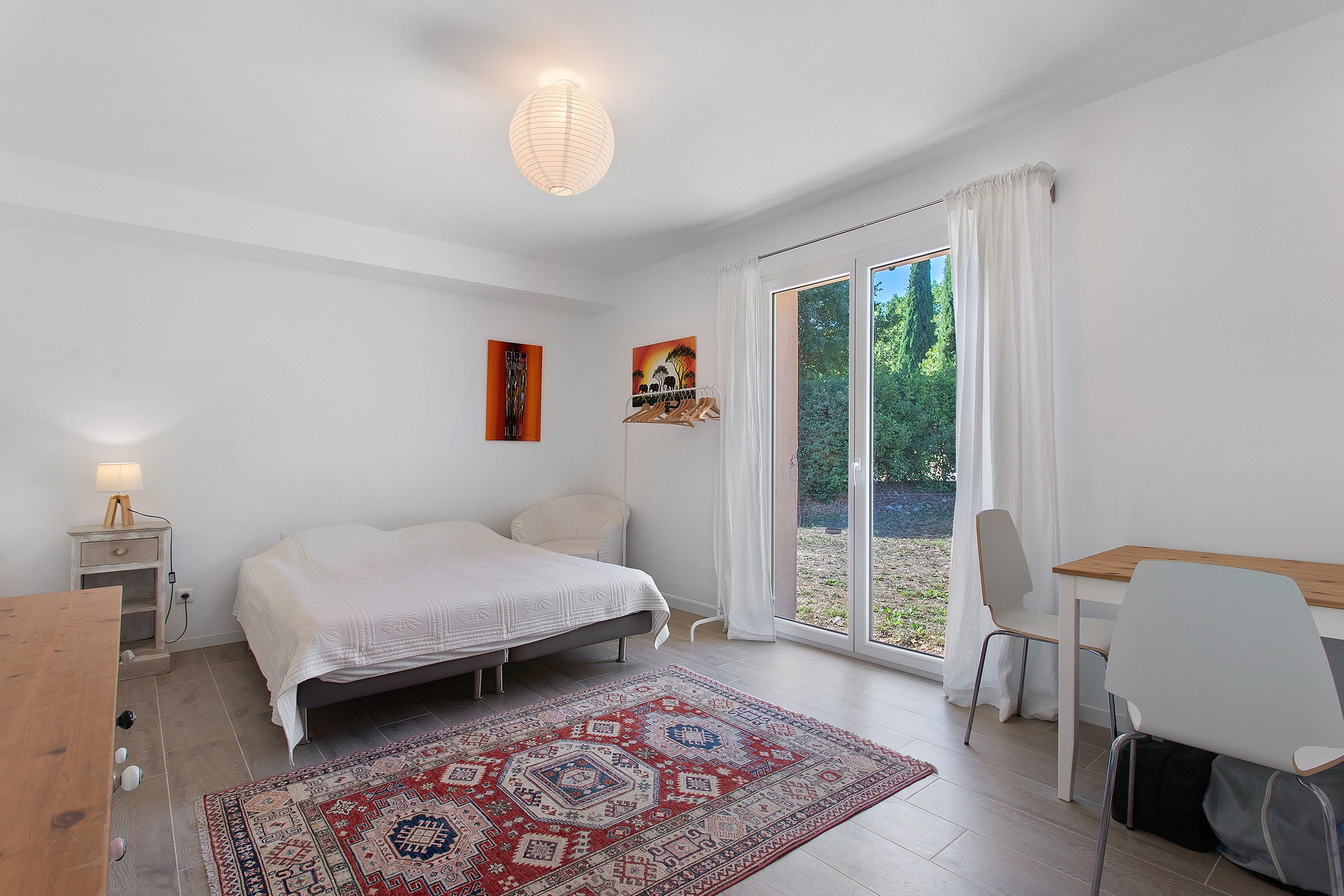 Un dormitorio con cama, escritorio, silla, alfombra y ventana con cortinas.