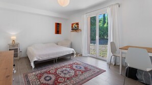 Un dormitorio con cama, escritorio, silla, alfombra y ventana con cortinas.
