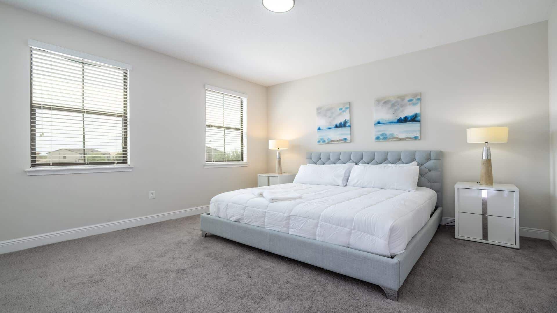 A bedroom with a bed, two bedside tables, a window, and artwork on the wall.