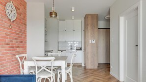 A modern kitchen with white cabinets, a dining table with chairs, and a blue sofa. - RentPlanet - Apartament Sucha (Gdańsk)