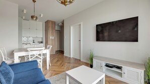 A modern living room with a blue sofa, white coffee table, and a TV stand. - RentPlanet - Apartament Sucha (Gdańsk)