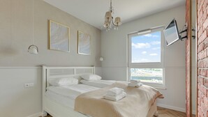 A bedroom with a bed, a window with a view, a chandelier, and artwork on the wall. - RentPlanet - Apartament Sucha (Gdańsk)