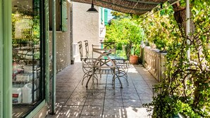 A patio with a table and chairs, surrounded by potted plants and a thatched roof. - Maison piscine à Anduze (Anduze)