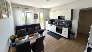 Ett modernt kök med vita skåp, en matplats med ett glasbord och en soffa med dekorativa kuddar.