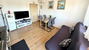 Ett vardagsrum med en soffa, en tv, ett matbord med stolar, ett soffbord och konstverk på väggarna.