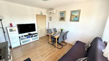 A living room with a sofa, a TV, a dining table with chairs, a coffee table, and artwork on the walls.