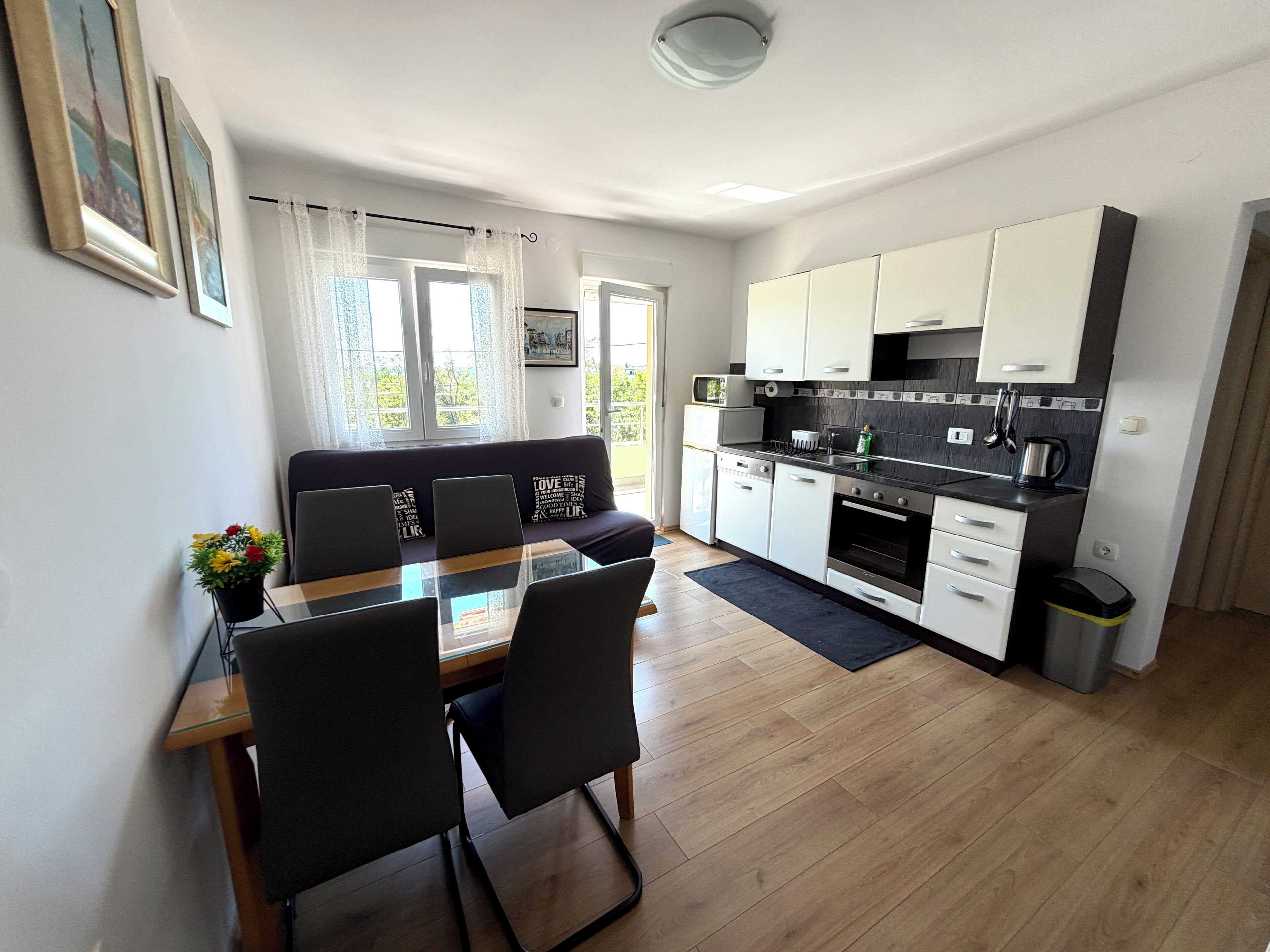 A modern kitchen with white cabinets, a dining table with chairs, and a sofa.