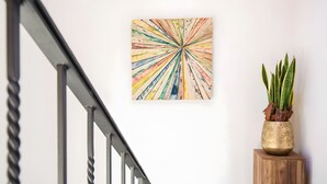 Una escalera con barandilla de metal, un cuadro abstracto colorido en la pared y una planta en maceta con hojas verdes.
