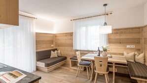Una habitación acogedora con detalles de madera, una mesa de comedor con sillas, un banco y una ventana con cortinas translúcidas.