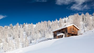 Une cabane en bois sur une pente enneigée, sous un ciel bleu dégagé.