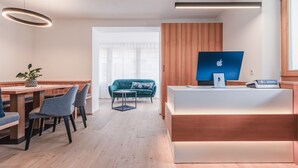 Un moderno mostrador de recepción con una computadora, un área de estar con sofá y sillones, y una mesa de comedor con sillas.