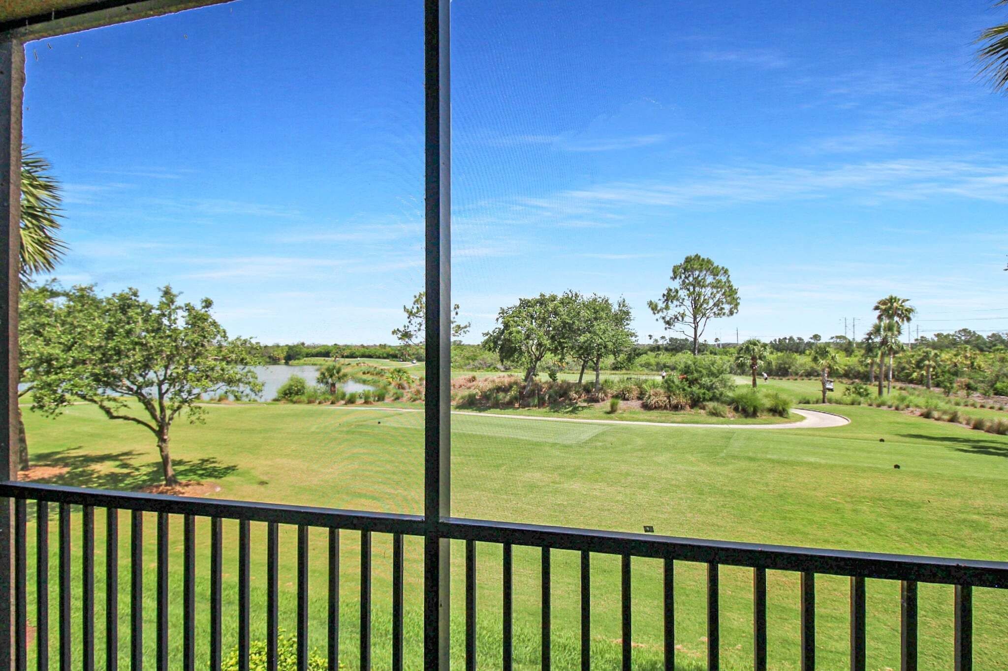 Blick auf einen Golfplatz mit einem Gewässer, Bäumen und blauem Himmel.