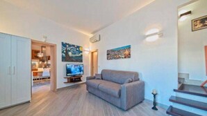 Een moderne woonkamer met een bank, een flatscreen televisie, kunstwerken aan de muur en een trap.