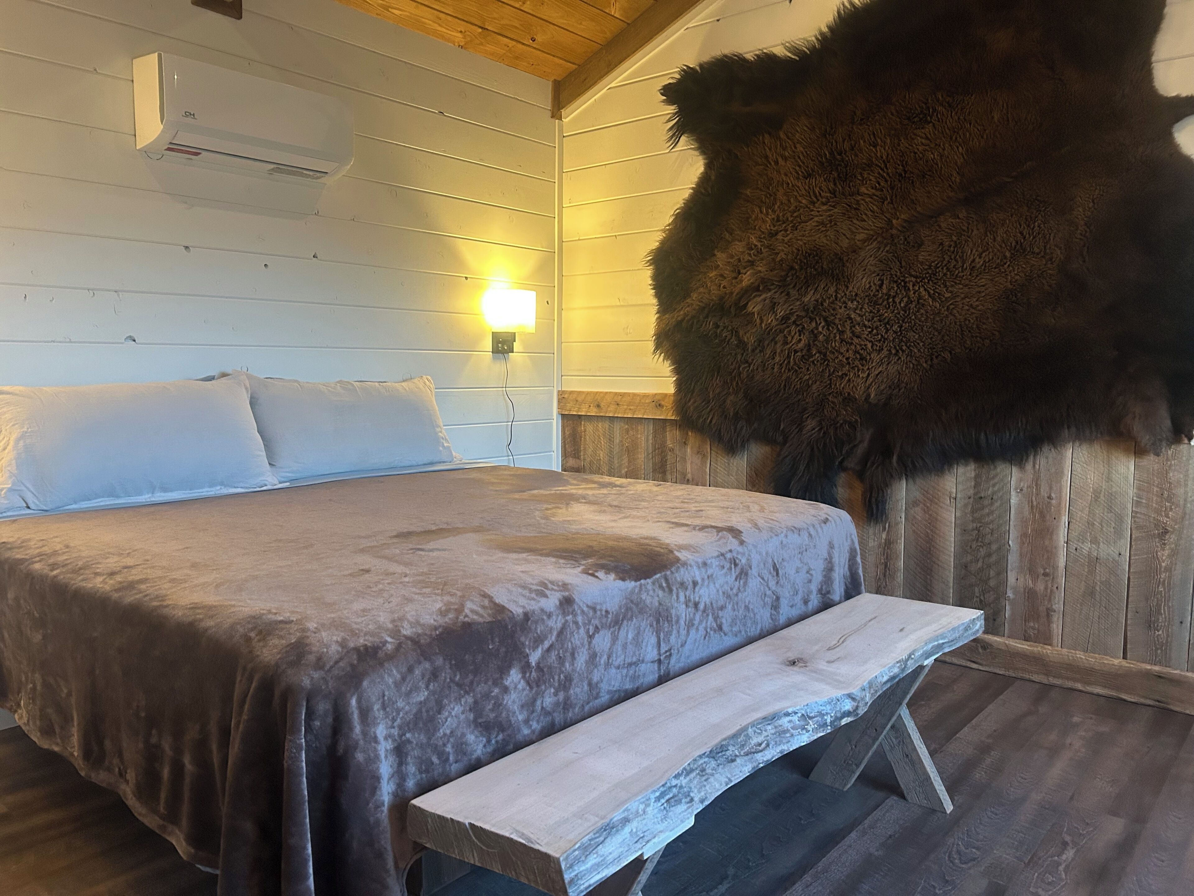 A bed with a bench, a wall-mounted light, and a fur rug.