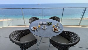 Ein runder Tisch mit Korbstühlen auf einem Balkon mit Blick auf das Meer.