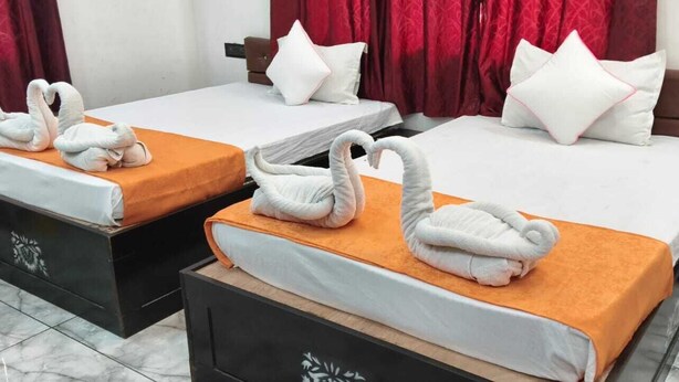 Two beds with white linens and orange bedspreads, each adorned with a white swan towel.
