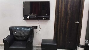 A room with a black leather armchair, a small ottoman, a TV mounted on the wall, and a dark wooden door.
