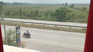 A highway with a motorcycle passing by, a signboard for a hotel, and a rural landscape in the background.